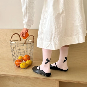 Detail of pink calf-high socks with black bows paired with black flat dress shoes