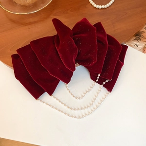 Detail of burgundy velvet bow hair clip with three-layer pearl tassel chains on white desk