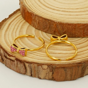Close-up of gold bow rings with pink zircon on natural wood display background