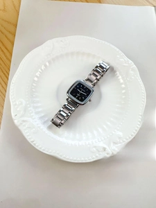 Macro shot of a square silver stainless steel watch with a black dial on a porcelain plate