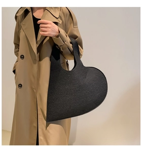 Detail of a minimalist black heart-shaped felt handbag held by a model in a trench coat