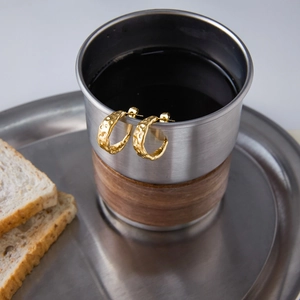 Close-up of gold stainless steel C-hoop earrings with hammered texture on a metal cup