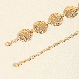 Detail view of gold metal waist chain featuring hammered texture discs and lobster clasp