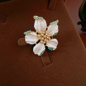 Détail d'une broche fleur vintage avec émail blanc, plaqué or et perles turquoise