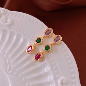 Vintage gold earrings with oval purple, emerald, and ruby stones on a velvet background