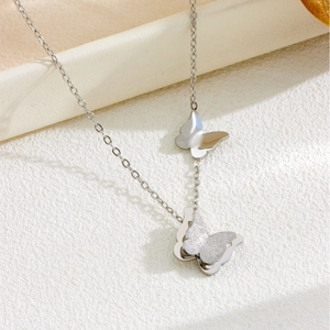 Minimalist silver butterfly necklace with dual matte and polished pendants on book