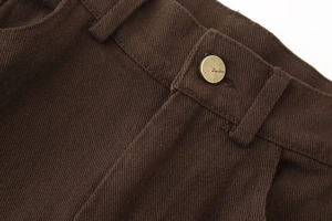 Makroaufnahme von dunkelbraunem Twill-Stoff und Messingknopf-Detail an der Damen-Hose