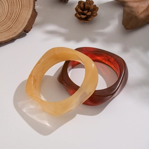 Dettaglio di ampi bracciali irregolari in resina con finiture ambra e tartaruga