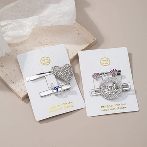 Detail of silver rhinestone hair clips including heart shape and NY logo on marble backdrop