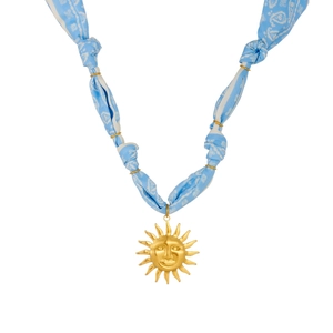 Detail of golden sun pendant on light blue patterned ribbon necklace with metal rings