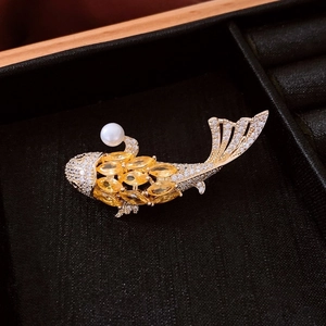 Macro shot of 18k gold plated fish brooch with yellow gems and pearls on black velvet