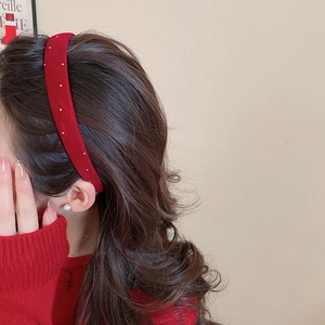 Detail view of red velvet headband with white pearl accents worn on long wavy brown hair