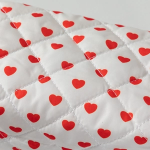 Detailed macro view of white quilted cotton fabric with small red heart pattern