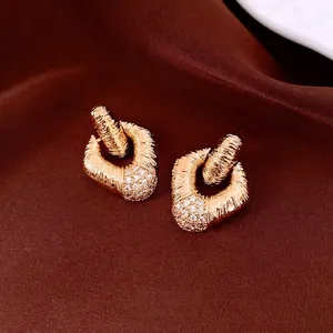 Vintage style gold earrings with hammered texture and paved zircon diamonds on satin background