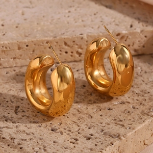 Detailed view of chunky golden C-shaped hoop earrings on a beige natural stone surface