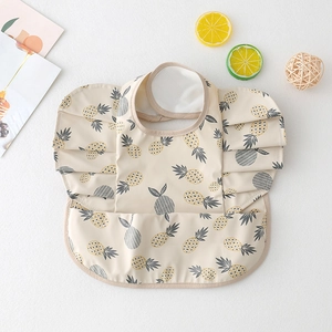 Detail view of beige baby bib with pineapple print, waterproof pocket and ruffle sleeves