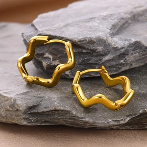 Detail showing gold irregular wave square hoop earrings on a textured stone surface