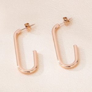 Vue macro de boucles d'oreilles en U en or rose sur fond de tissu texturé rose