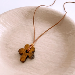 Macro detail of a tiger eye flower pendant with brown cord on a ceramic plate