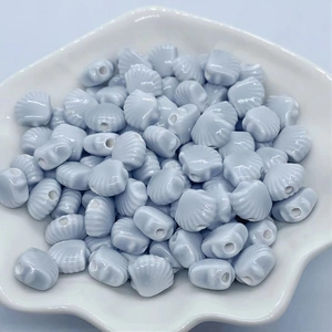 Macro view of light blue shell-shaped ceramic beads for jewelry making in a white dish