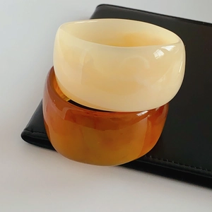 Detail of cream white and amber orange wide resin bangles on black leather clutch