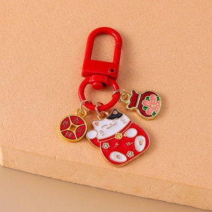 Lucky cat keychain with red fortune bag and copper coin charm on a beige textured base