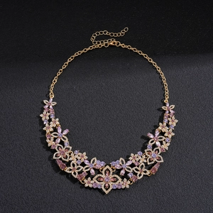Detail of gold floral necklace with purple and pink crystals on black background