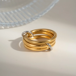 Macro detail of intertwined gold rings with silver link connectors on a minimalist surface