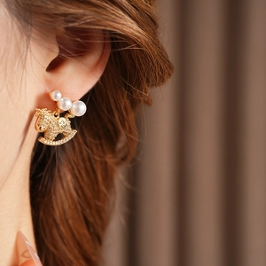 Gros plan sur des boucles d'oreilles cheval à bascule dorées, strass et trois perles