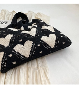 Flat lay of a black knit tote bag featuring white heart patterns on a fabric background