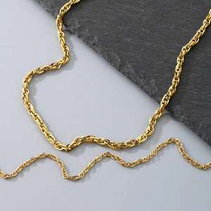 Detail of twisted rope chains in shiny gold finish on a modern minimalist stone background