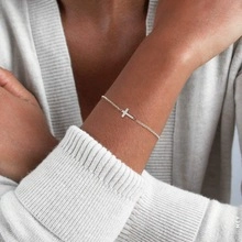 Gros plan d'un bracelet croix délicat en argent porté au poignet avec un pull blanc