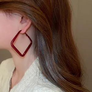 Deep red oversized geometric square hoop earrings worn by a model in a side profile view