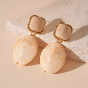 Detail of beige resin marble earrings with gold metal trim on a textured stone surface
