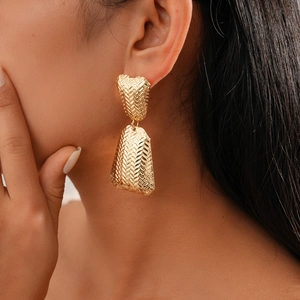 Close-up of a model wearing golden woven texture drop earrings with a metallic finish