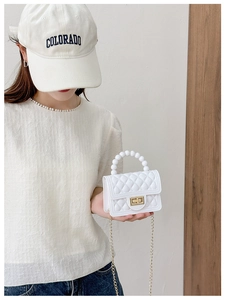 Detail of white PVC jelly bag with quilted texture, pearl handle and gold chain strap