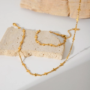 Minimalistische Goldene Kreuzkette und Armband-Set präsentiert auf Natursteinsockel