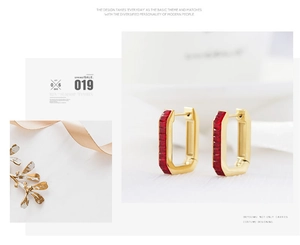 Close-up of gold rectangular hoop earrings set with vertical baguette-cut red crystals