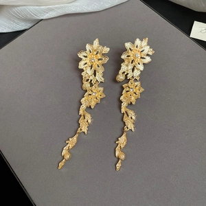 Détail de boucles d'oreilles pendantes fleurs dorées sur soie grise et boîte à bijoux