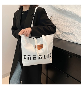 Close-up of white canvas tote bag featuring black letter print and brown leather tag