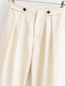 Close-up of beige high-waisted trousers featuring double buttons and pleated details