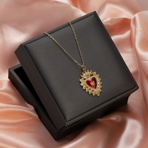 Detail of a red enamel heart crown necklace in a black gift box on pink silk