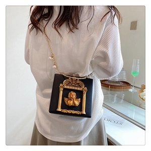 Detailed view of Baroque gold angel relief and pearl chain on black crossbody bag