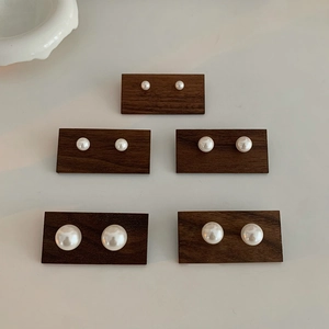 Detail shot of five pairs of pearl stud earrings in varying sizes on dark wood display