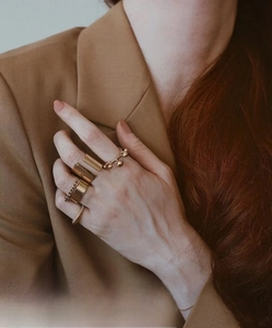 Set of gold letter rings including chain and twisted bands worn over a brown blazer