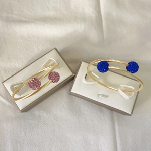 Détail de joncs torsadés dorés avec embouts en cristal rose et bleu dans un écrin à bijoux