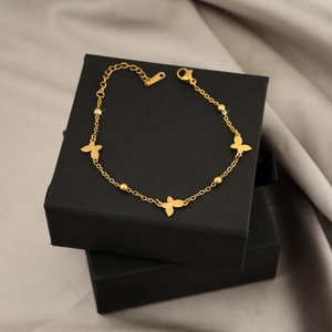 Detailed close-up of golden titanium steel butterfly charm bracelet on a black box