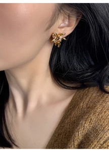 Close-up of 18K gold-plated tiger eye flower earrings worn by a model with brown sweater