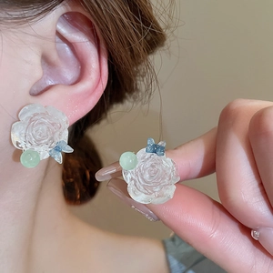 Detailed close-up of a resin rose earring with blue ribbon and green bead on a model