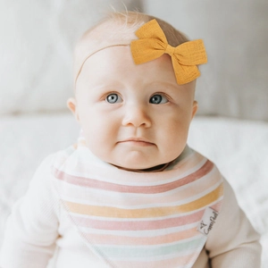 Close-up of baby mustard bow headband and rainbow striped cotton bib set on a baby
